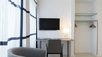 A modern hotel room with a desk, chair, television, and a walk-in closet.