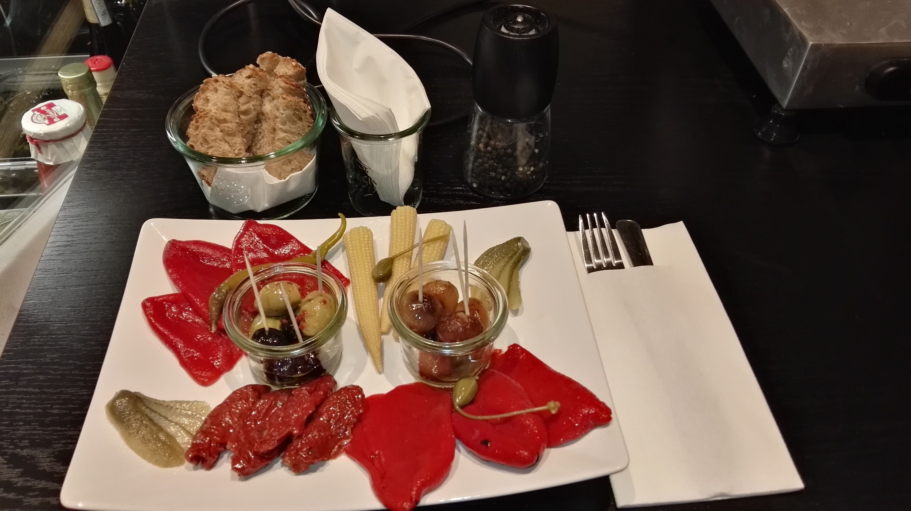 A plate with various foods including pickled vegetables, olives, and corn on the cob.