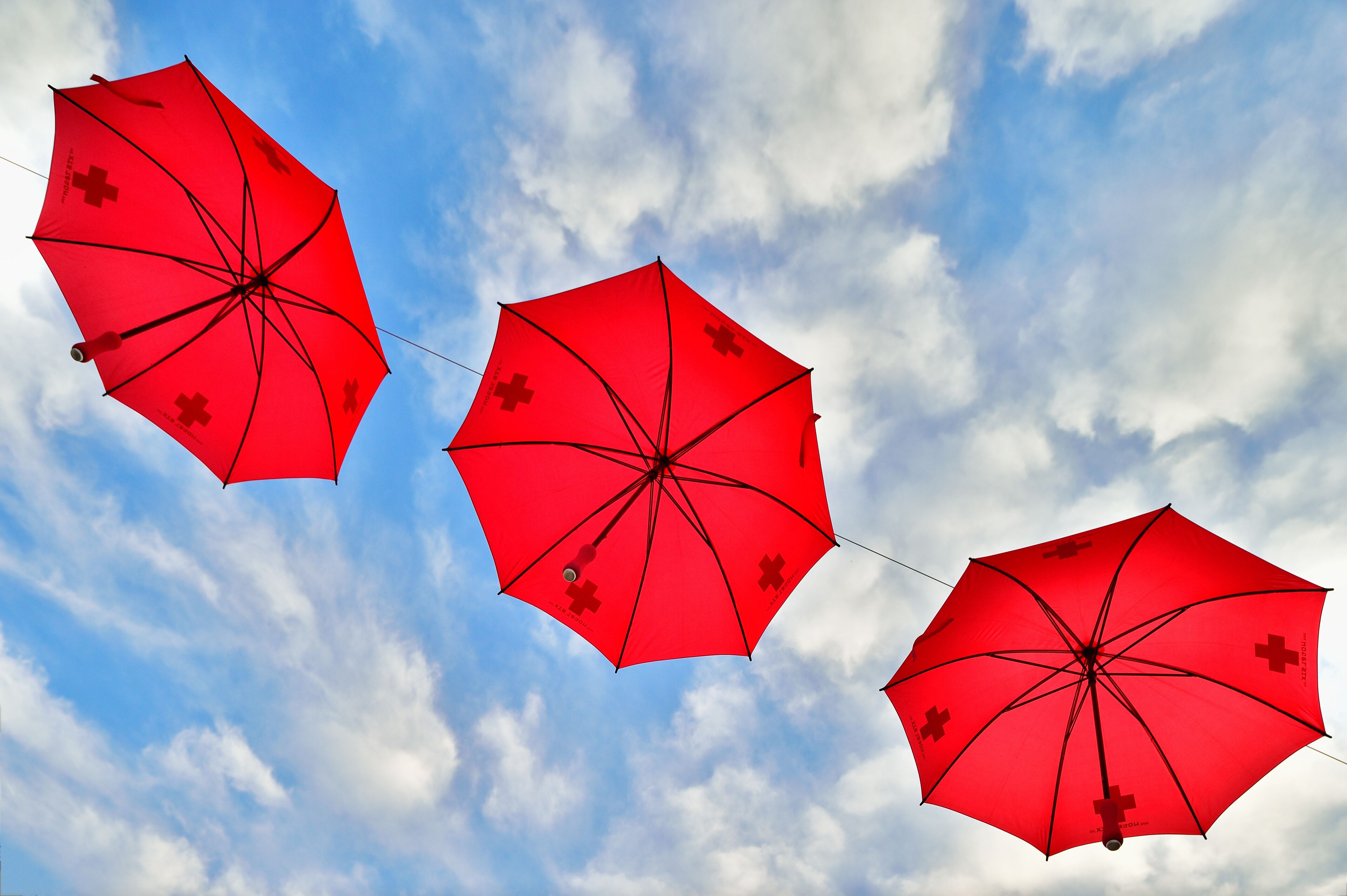 Drei rote Regenschirme vor einem bewölkten Himmel.
