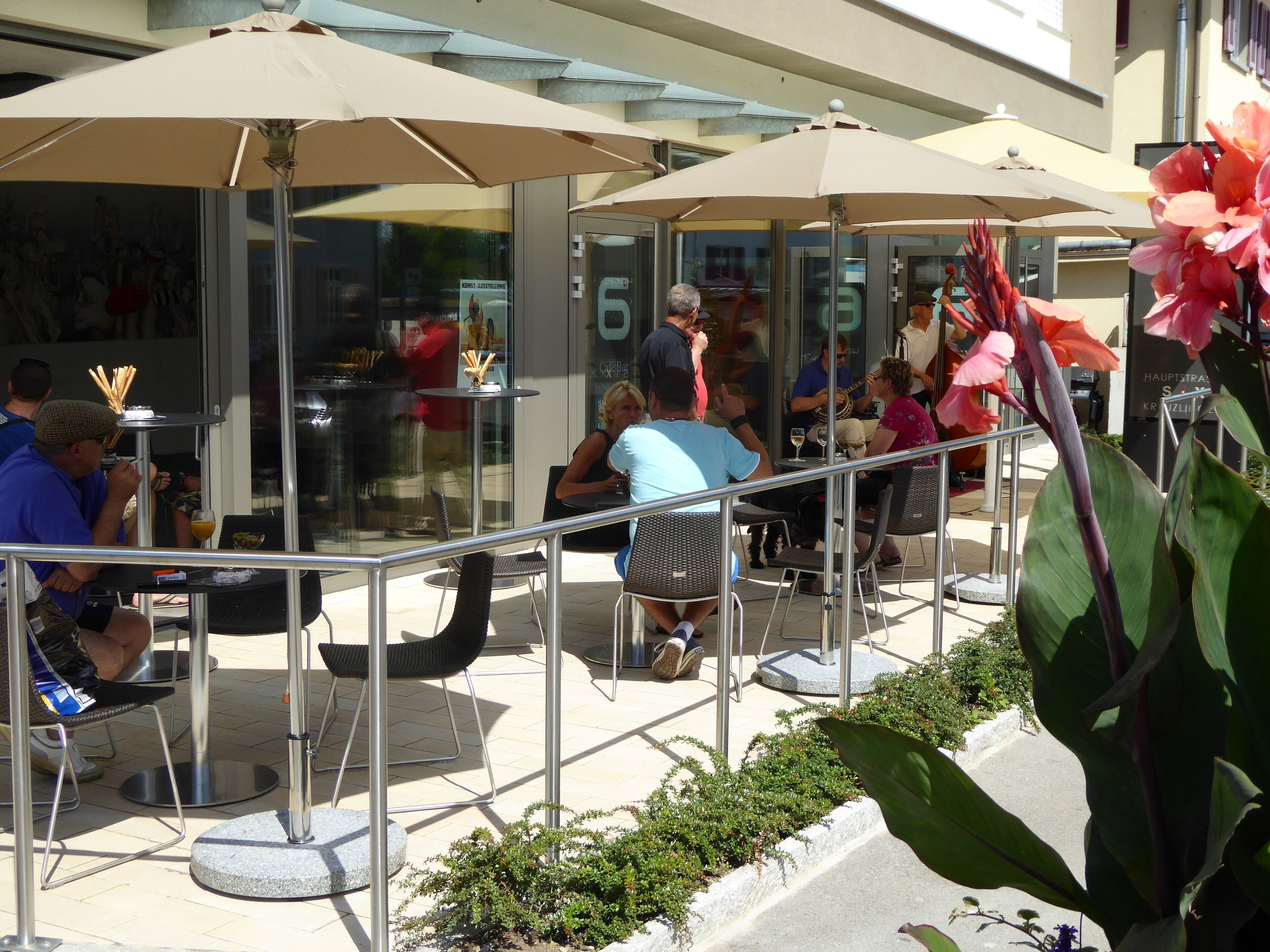Een terras met tafels en stoelen, parasols en een glazen gevel.