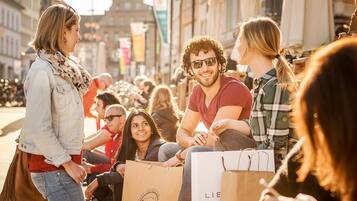 Un grupo de personas sentadas al aire libre, algunas con bolsas de compras.