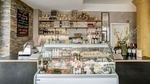 Una panadería con estanterías llenas de productos horneados, una vitrina de pasteles y un muro de ladrillo.