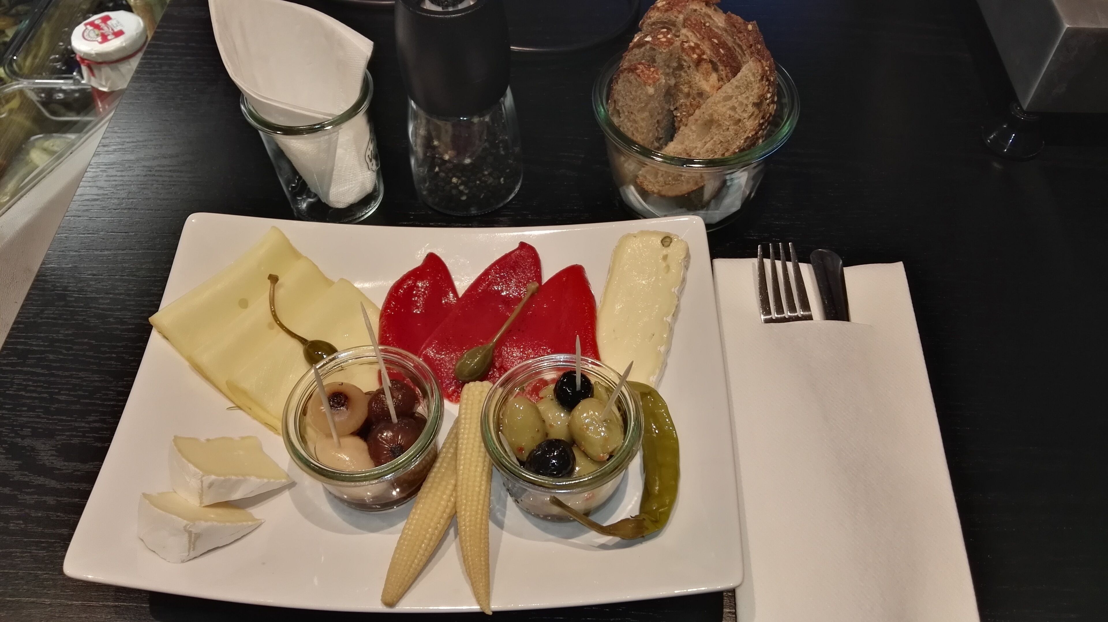 A plate with cheese, olives, and pickles on a table.
