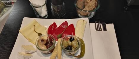 A plate with cheese, olives, and pickles on a table.