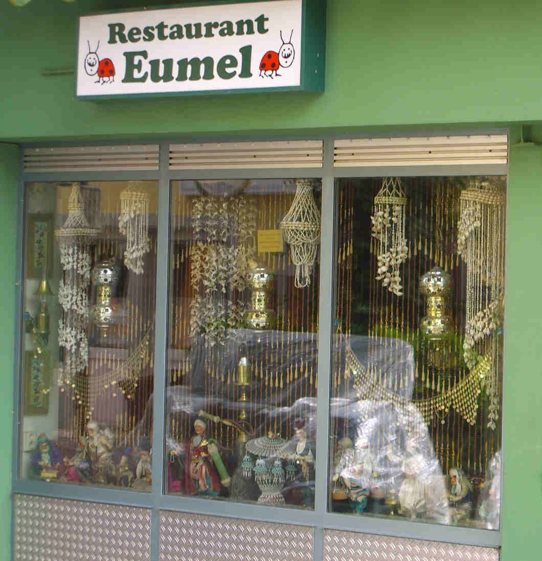 A restaurant named 'Eumel' with a sign above the window displaying various decorative items.