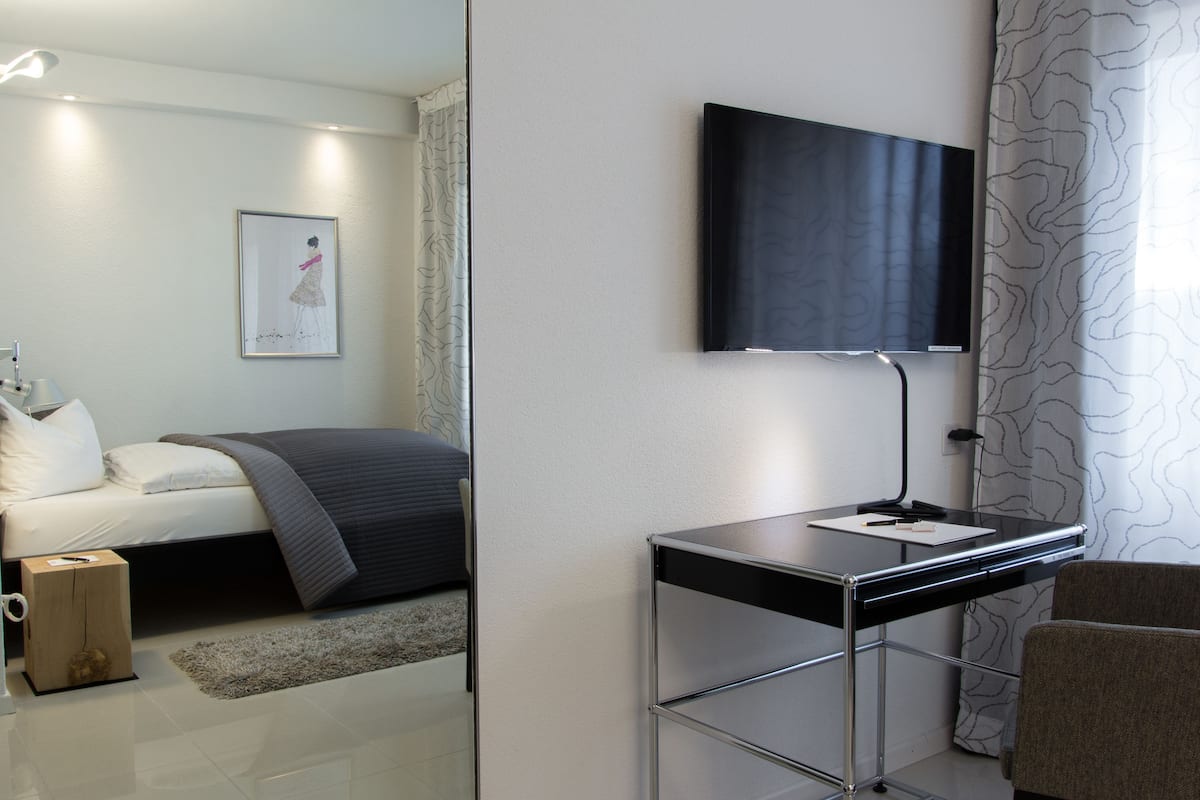 Quarto moderno com cama, mesa de cabeceira e televisão montada na parede.