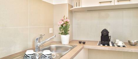 A modern kitchen with a stainless steel sink, two zebra-patterned mugs, a potted plant with pink flowers, a coffee maker, and a bowl on the countertop.