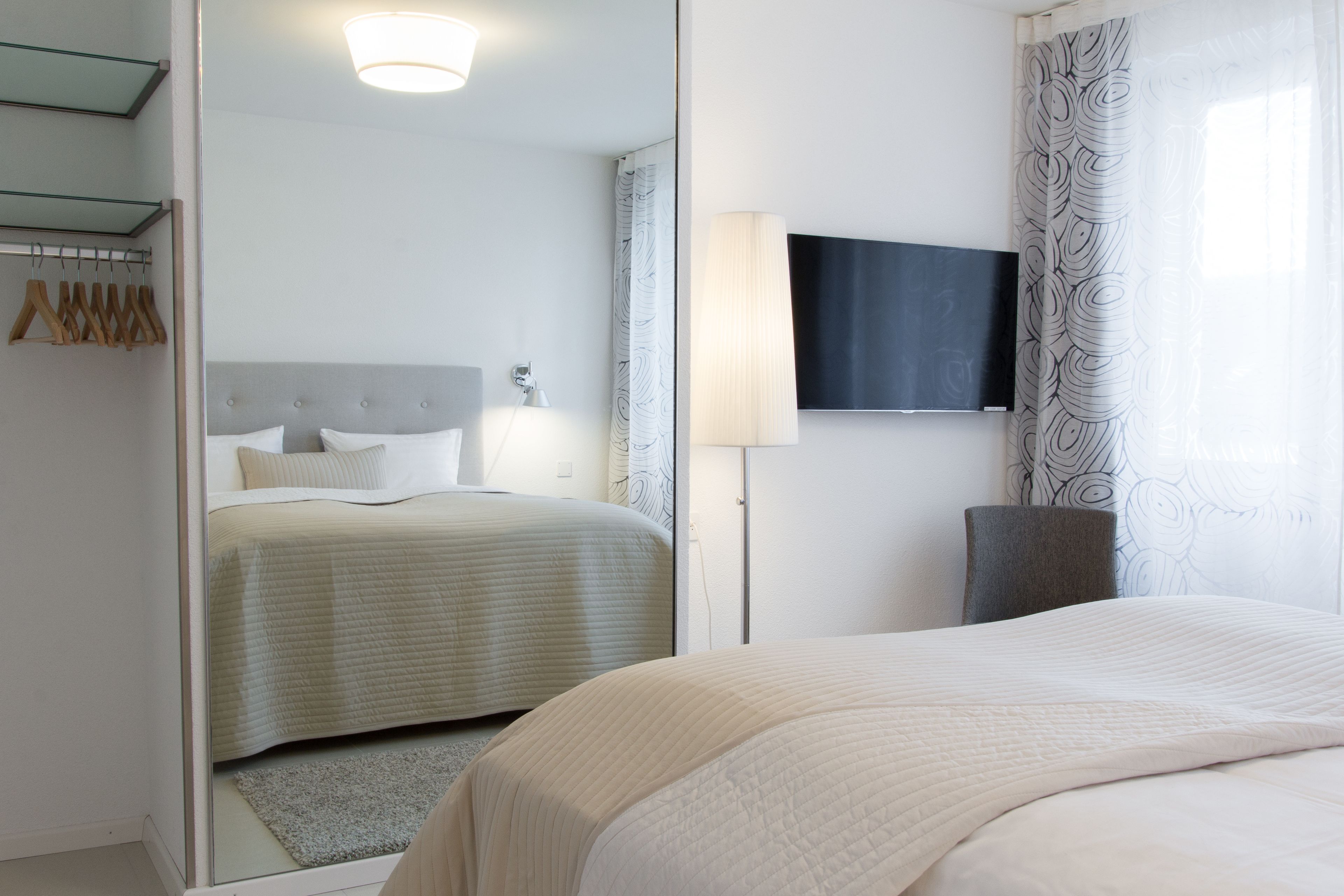 A bedroom with a bed, a bedside table, a lamp, a TV, and a mirror.