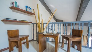 A room with a wooden table and two chairs, a staircase with blue balusters, and shelves with books and decorative items.