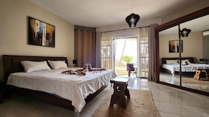 A spacious bedroom with a large bed, a small table, and a chair. There is a sliding glass door leading to an outdoor area.
