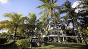 A modern building with a curved roof, surrounded by palm trees and a well-maintained lawn.
