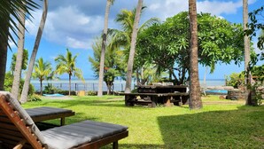 A tropical outdoor area with wooden lounge chairs, a picnic table, and a view of the ocean.