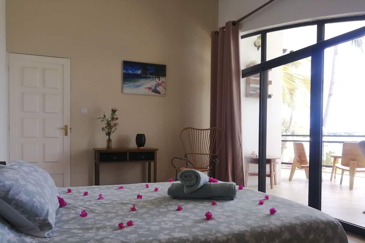 A bedroom with a bed, a night sky painting, a desk, a chair, and a balcony with chairs.
