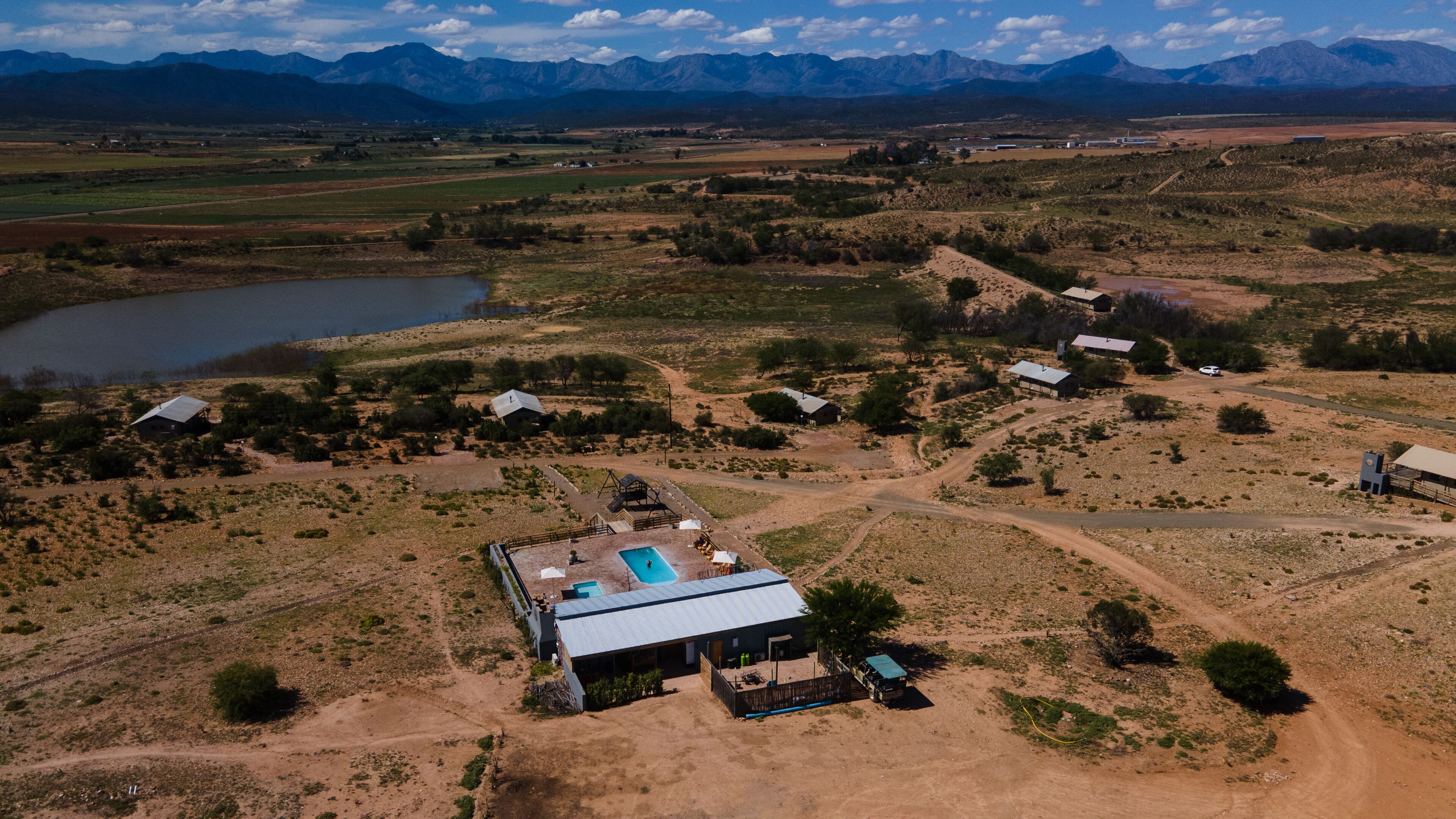 An aerial view of a rural property with a swimming pool, multiple cabins, and a large body of water.
