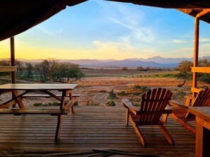 Una terraza de madera con mesa y sillas, con vistas a un paisaje desértico y montañas a lo lejos.