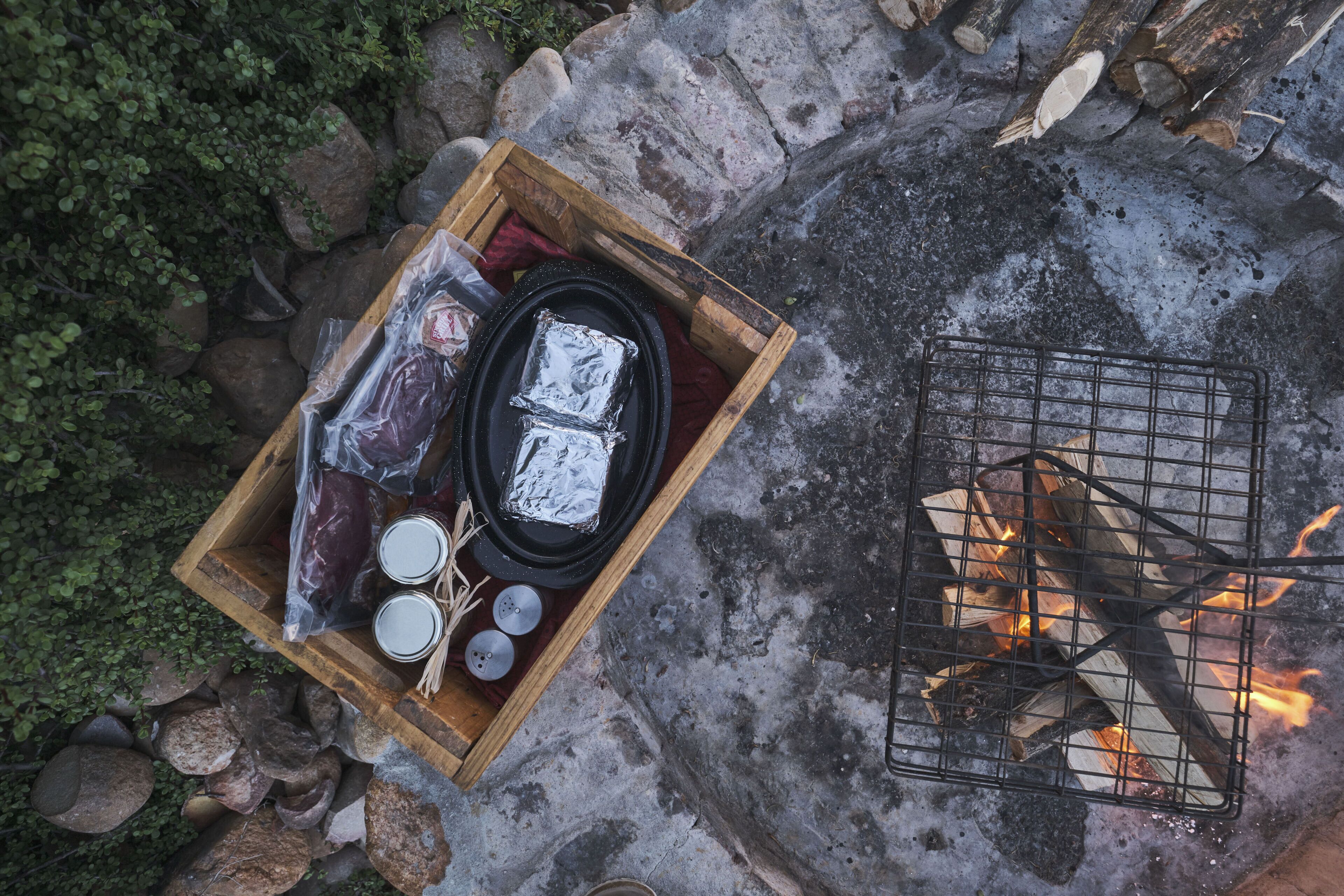 A wooden box with food items and a metal grill over a fire.