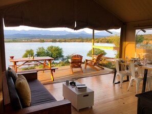 Une terrasse en bois avec une table et des chaises, donnant sur un lac, avec des montagnes en arrière-plan.