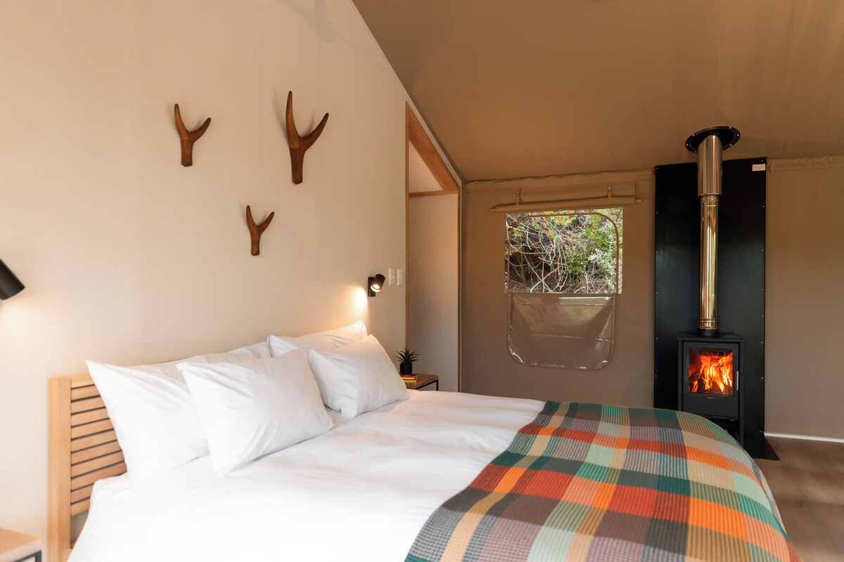 Een slaapkamer met een bed, een wandradiator en een raam met uitzicht op groen.