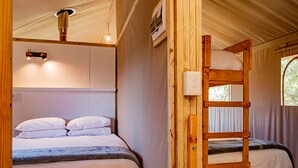 Een stapelbed met een houten trap en een enkel bed met hoofdeinde. Er is een plafondlamp en een airconditioning zichtbaar.