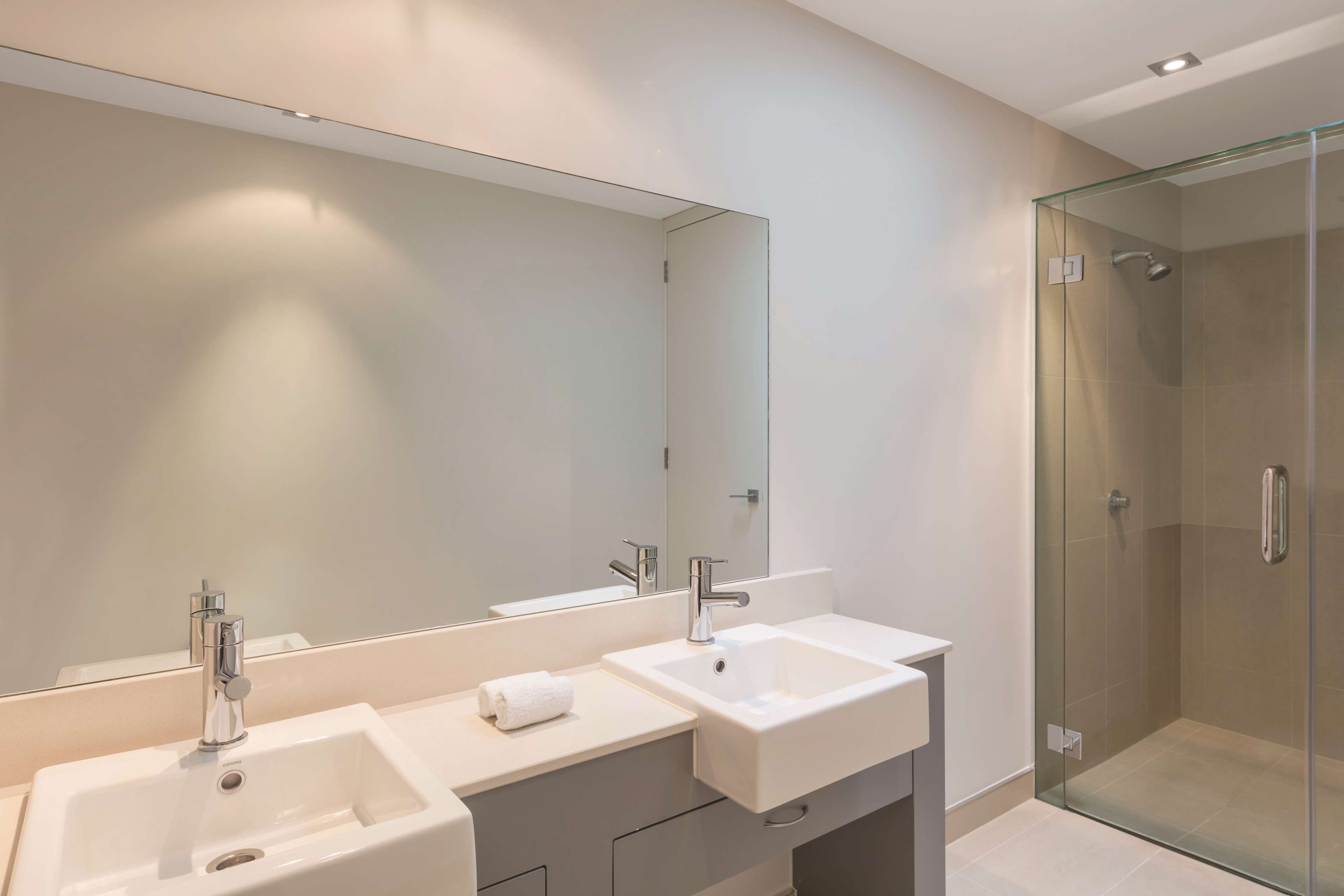 A modern bathroom with two sinks, a large mirror, and a glass-enclosed shower.