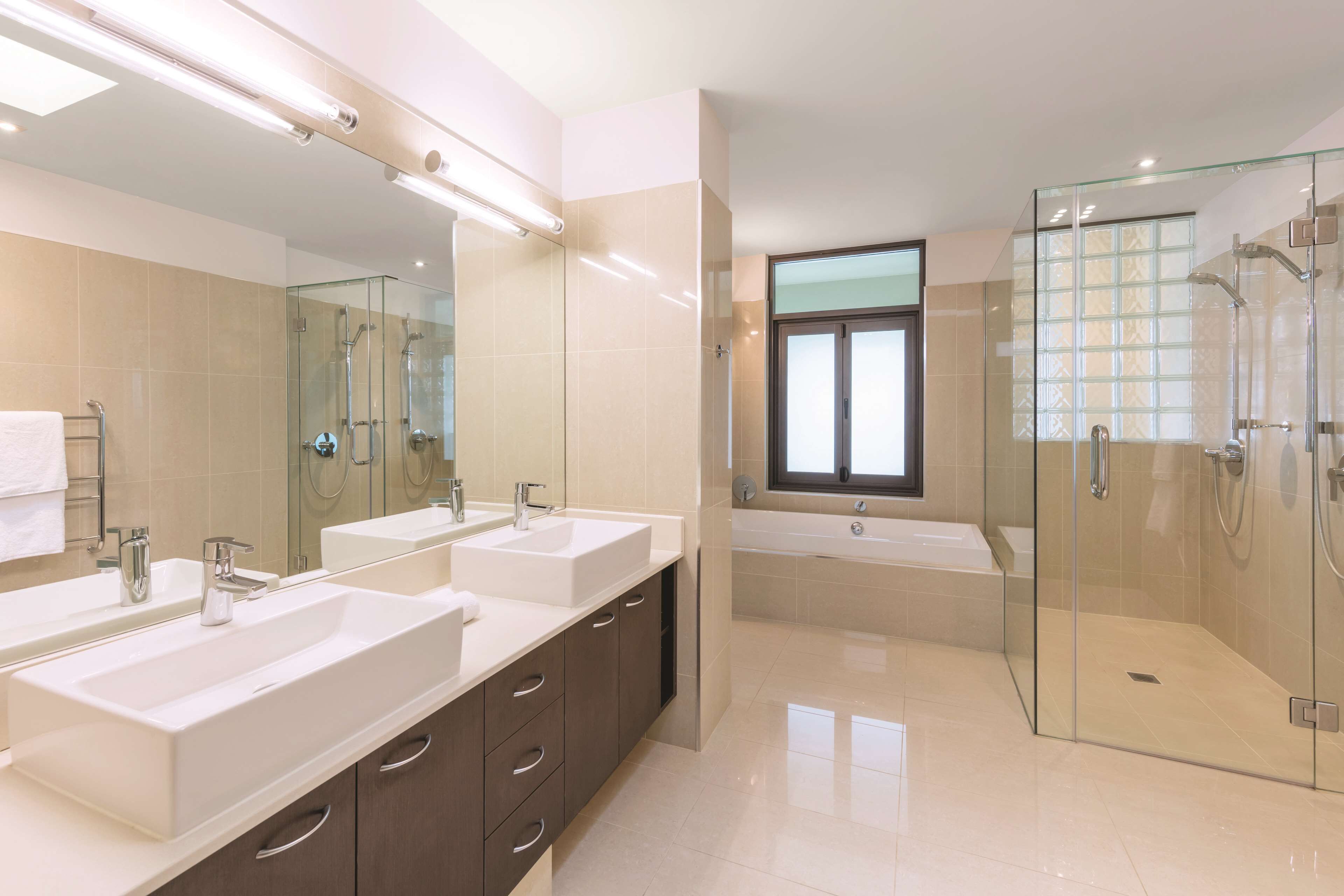 A modern bathroom with two sinks, a glass-enclosed shower, and a large mirror.
