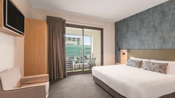 Quarto de hotel com uma cama grande, televisão de tela plana na parede, área de estar com uma poltrona e uma varanda com vista para a cidade.