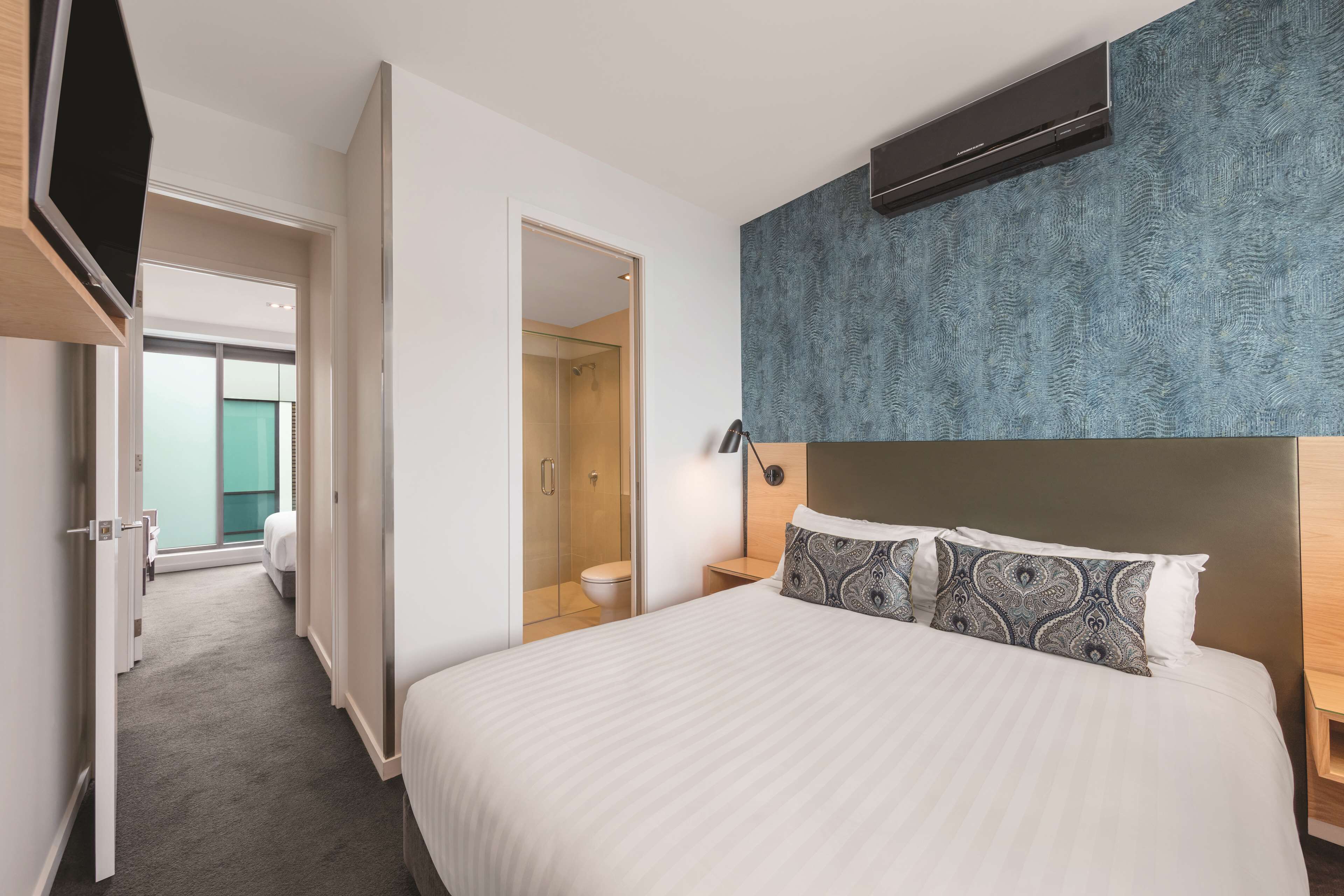 Ein Hotelzimmer mit einem großen Bett, einem begehbaren Kleiderschrank, einem Badezimmer mit Glasdusche und Blick auf die Stadt.