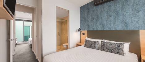 Ein Hotelzimmer mit einem großen Bett, einem begehbaren Kleiderschrank, einem Badezimmer mit Glasdusche und Blick auf die Stadt.