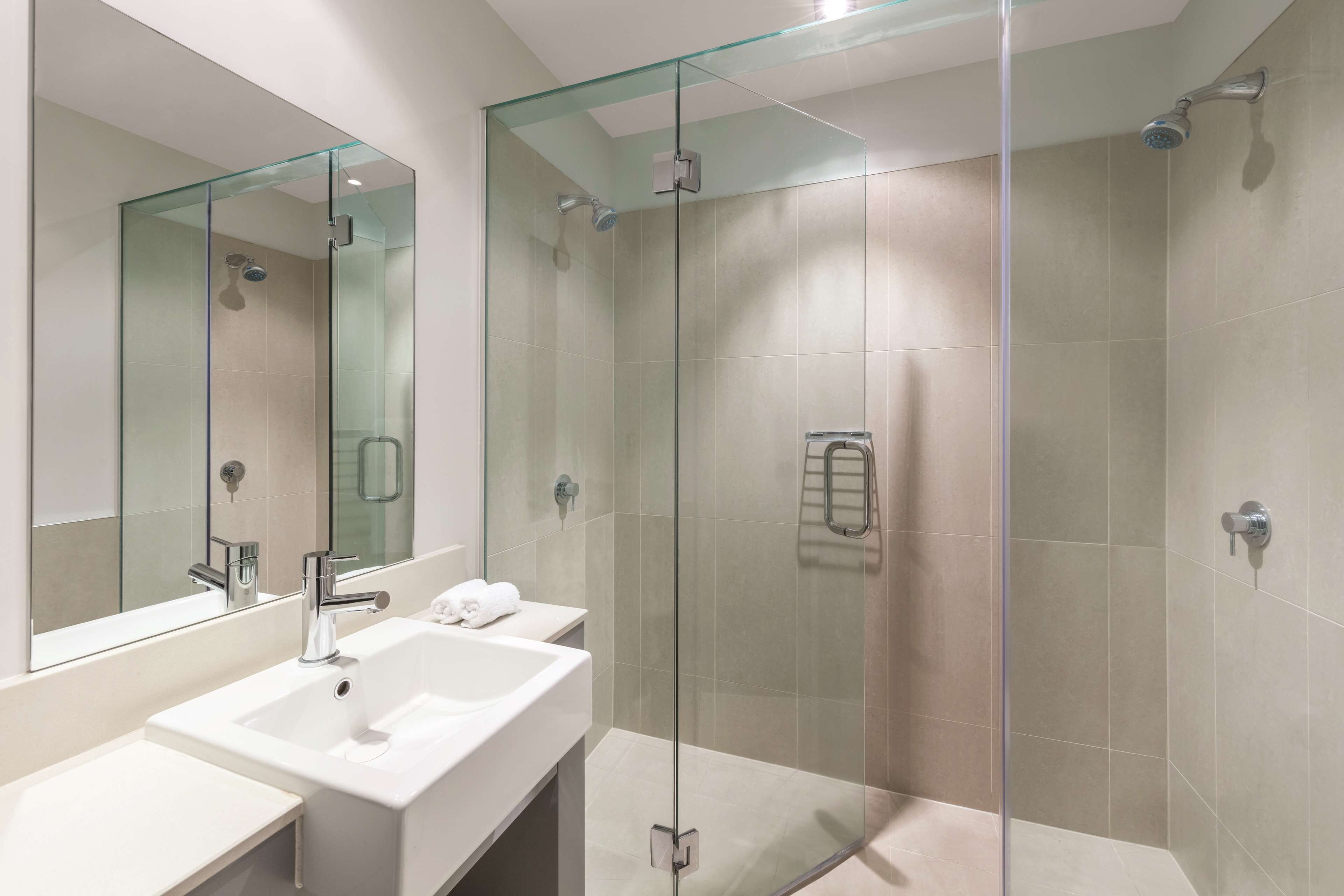 A modern bathroom with a glass-enclosed shower, a white sink, and a large mirror.