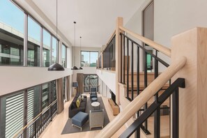 Un interior moderno con una escalera, ventanas amplias y una zona de estar con sofás y una mesa de centro.