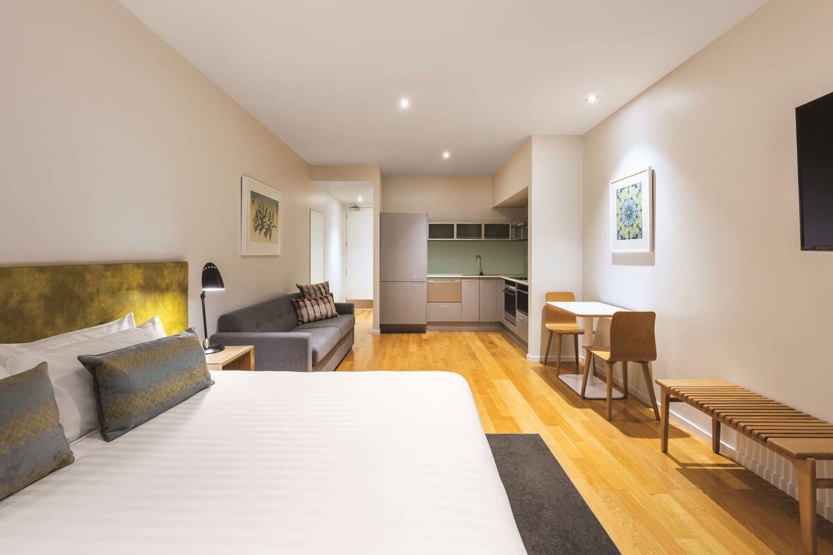 Ein modernes Hotelzimmer mit einem großen Bett, einer Couch, einem Esstisch mit Stühlen und einer Küchenzeile im Hintergrund.