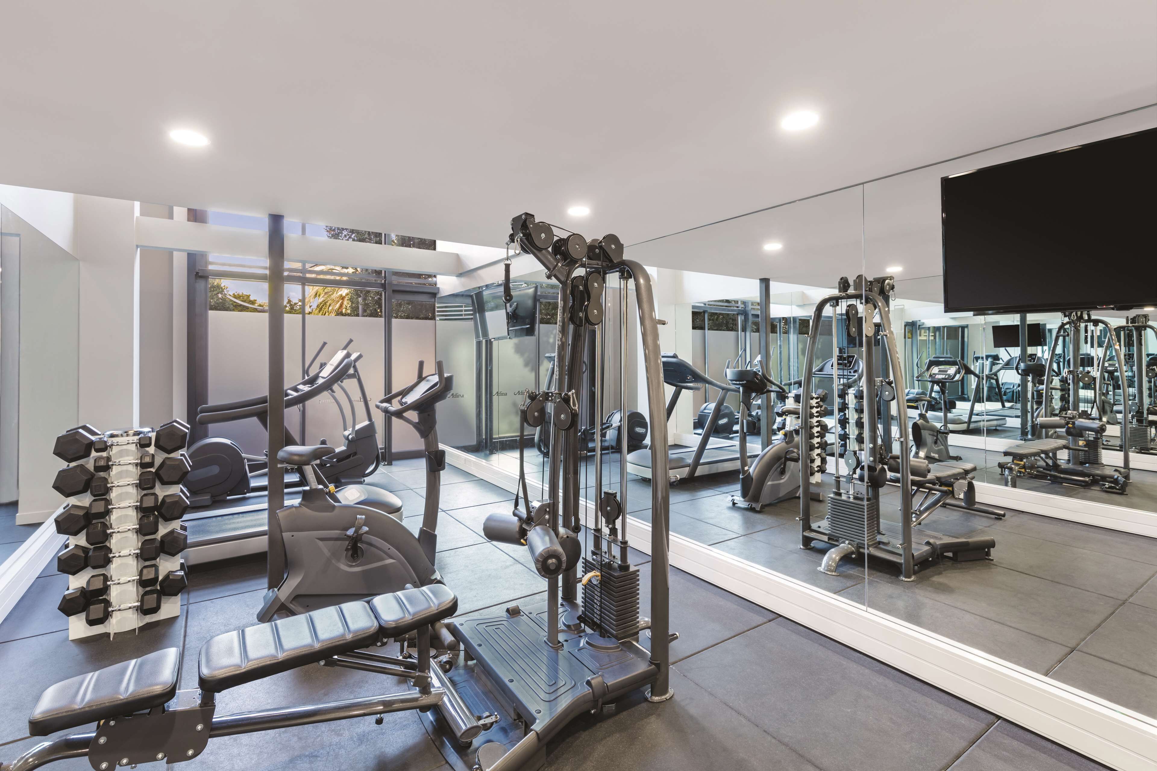 A modern gym with various exercise equipment, including dumbbells, a bench press, and a cable machine.