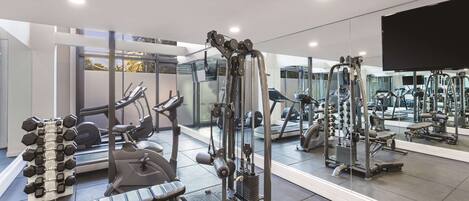 A modern gym with various exercise equipment, including dumbbells, a bench press, and a cable machine.