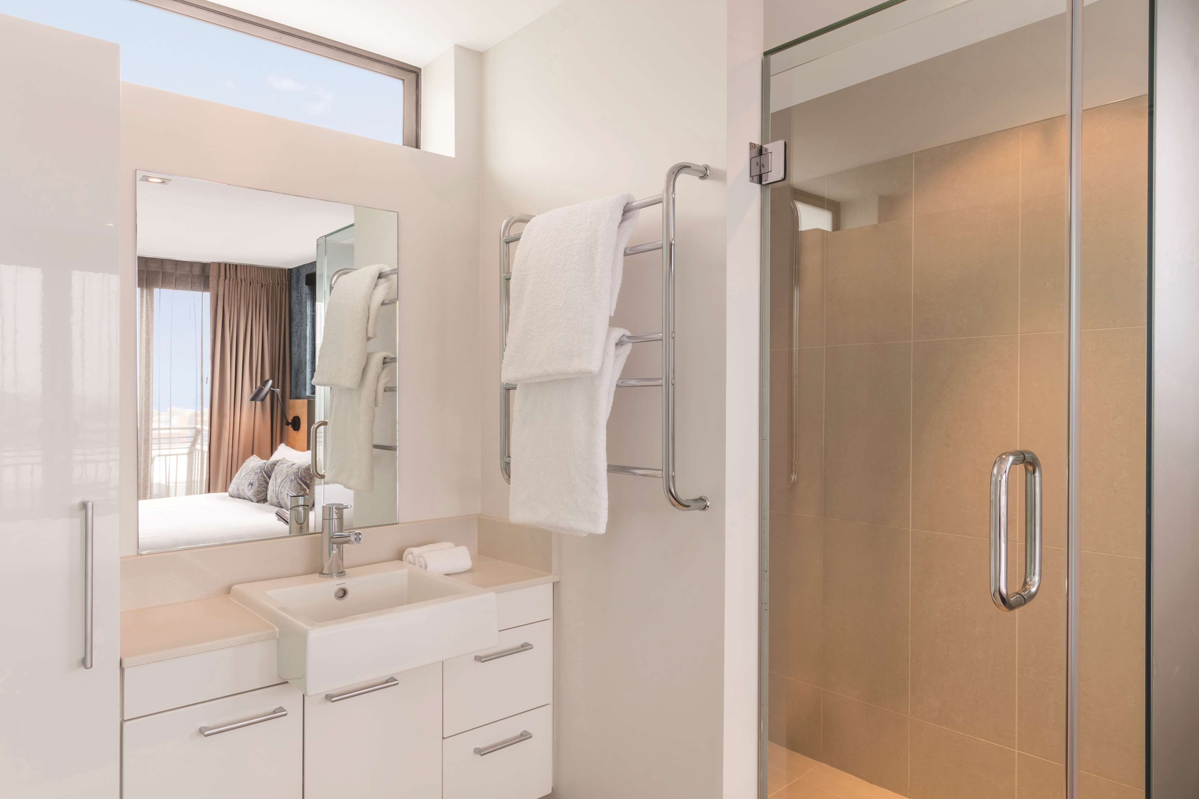 A modern bathroom with a large mirror, a sink, a towel rack, and a shower area.