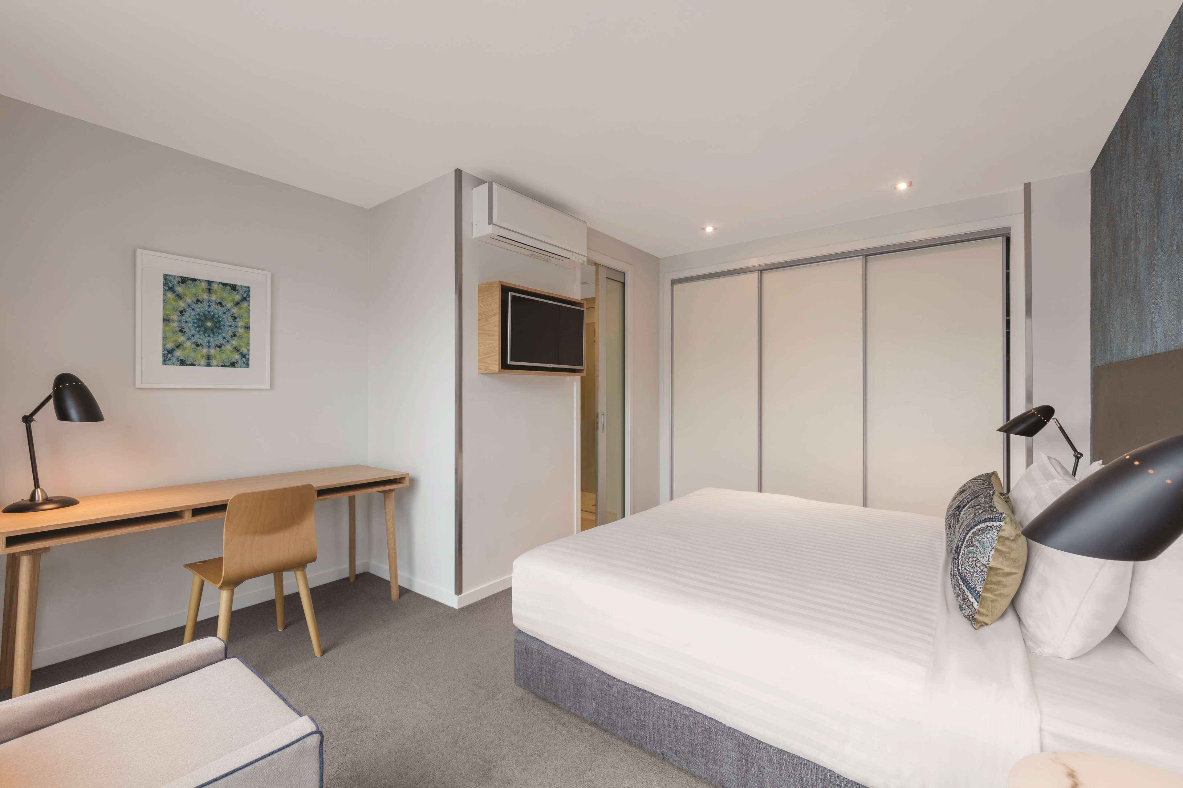 A modern hotel room with a bed, a desk, a chair, and a TV.