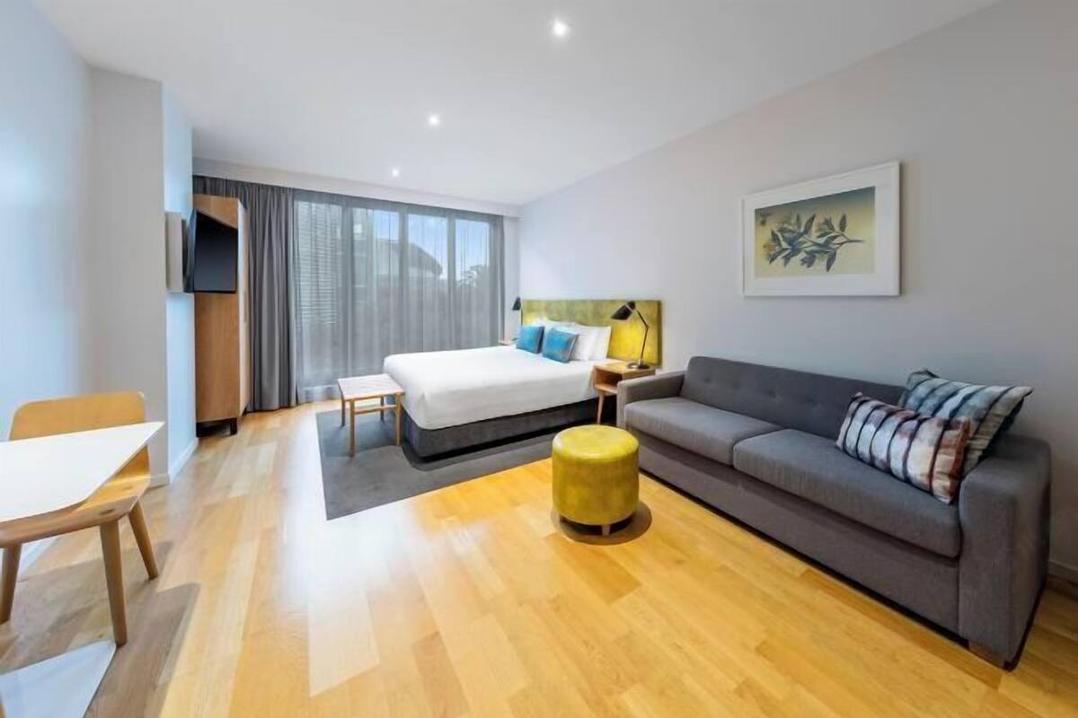Ein modernes Hotelzimmer mit Bett, Sofa, Fernseher, Kunstwerken und einem Essbereich.