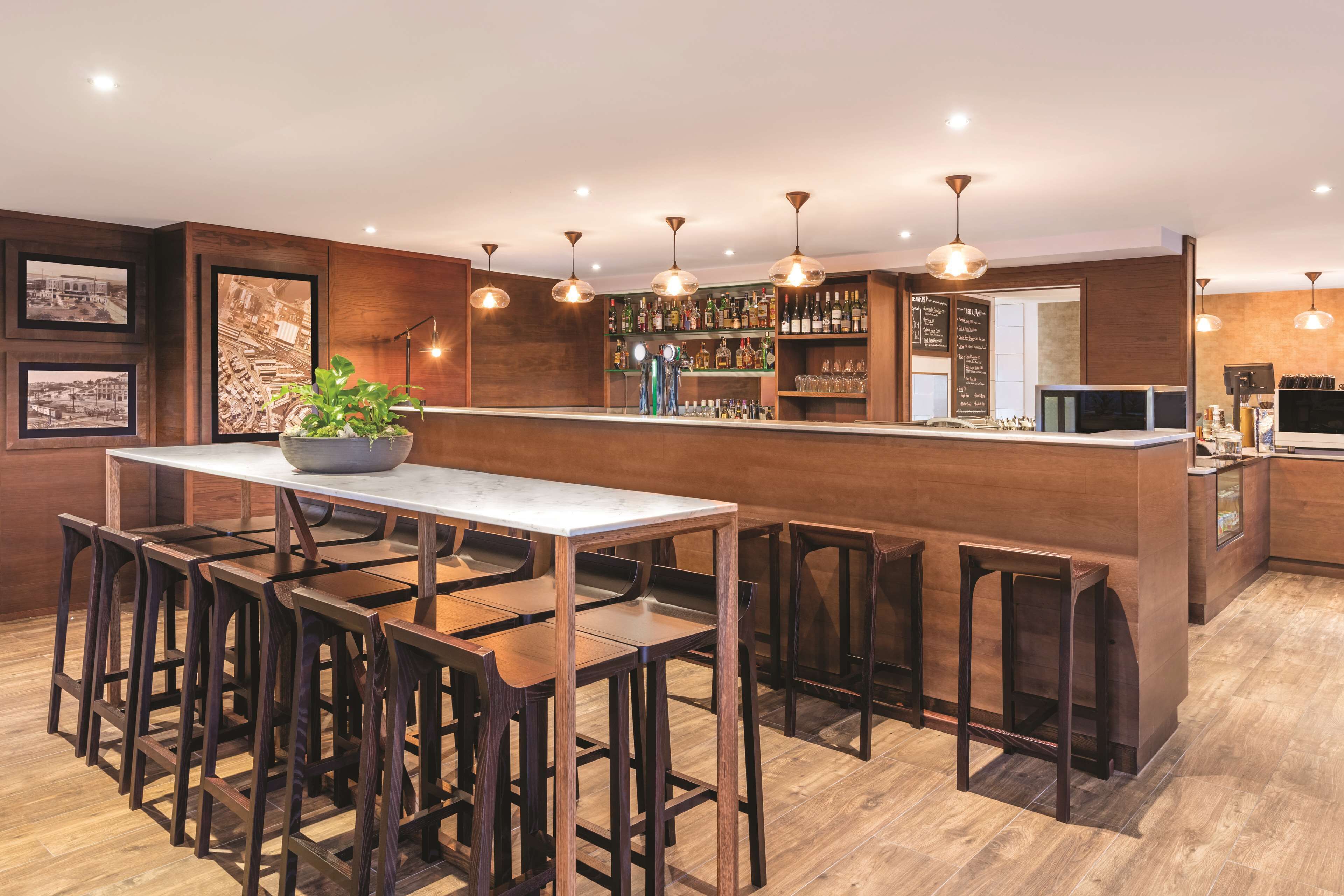 A modern bar area with wooden furniture, a bar counter, and a variety of bottles and glasses.