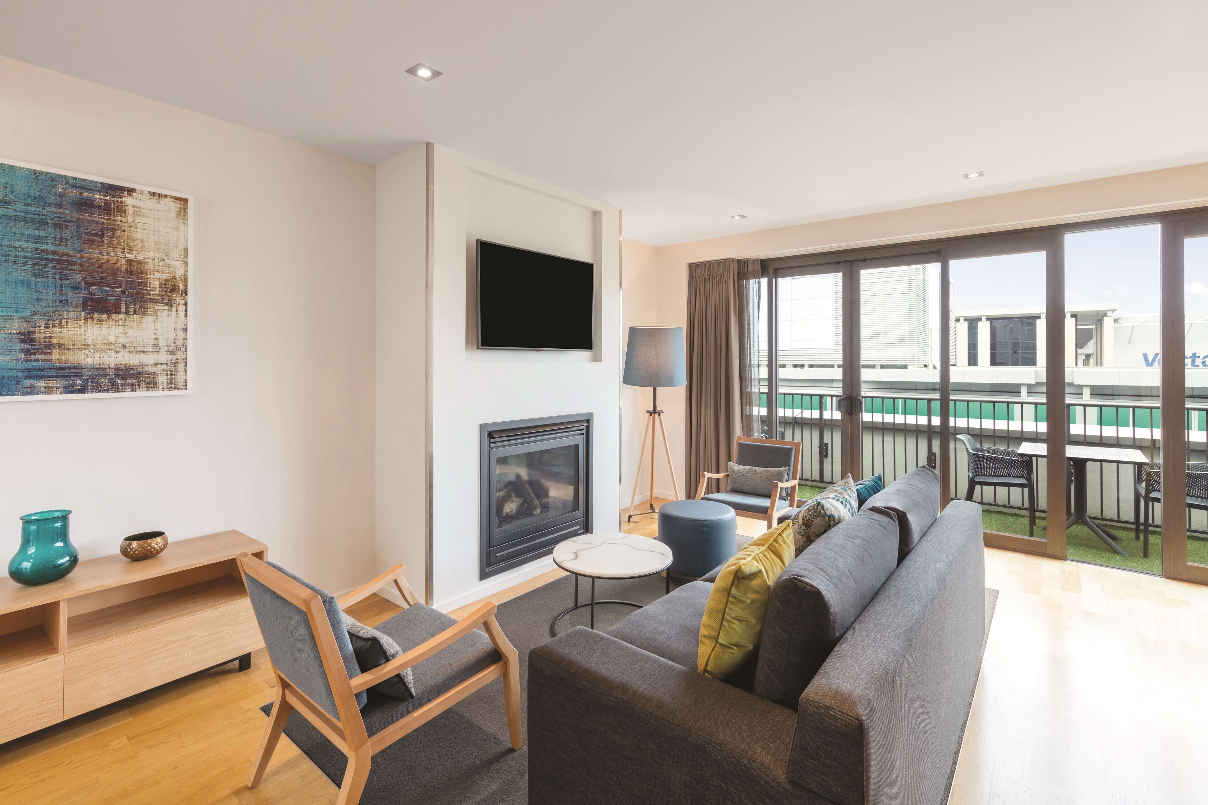 Un salon moderne doté d’une cheminée, d’un téléviseur à écran plat, d’un canapé, d’un coin repas avec des sièges extérieurs et d’un balcon offrant une vue sur les bâtiments.