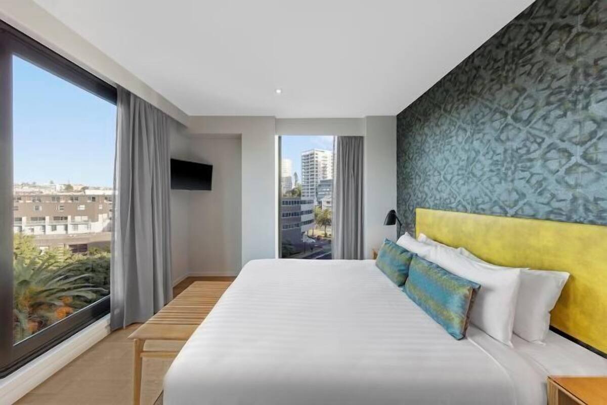 Ein modernes Hotelzimmer mit einem großen Bett, einem Fernseher und Blick auf die Stadtlandschaft.