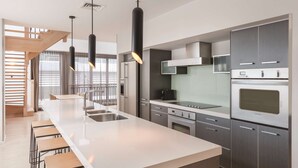 Een moderne keuken met een groot eiland, roestvrijstalen apparatuur en hanglampen.