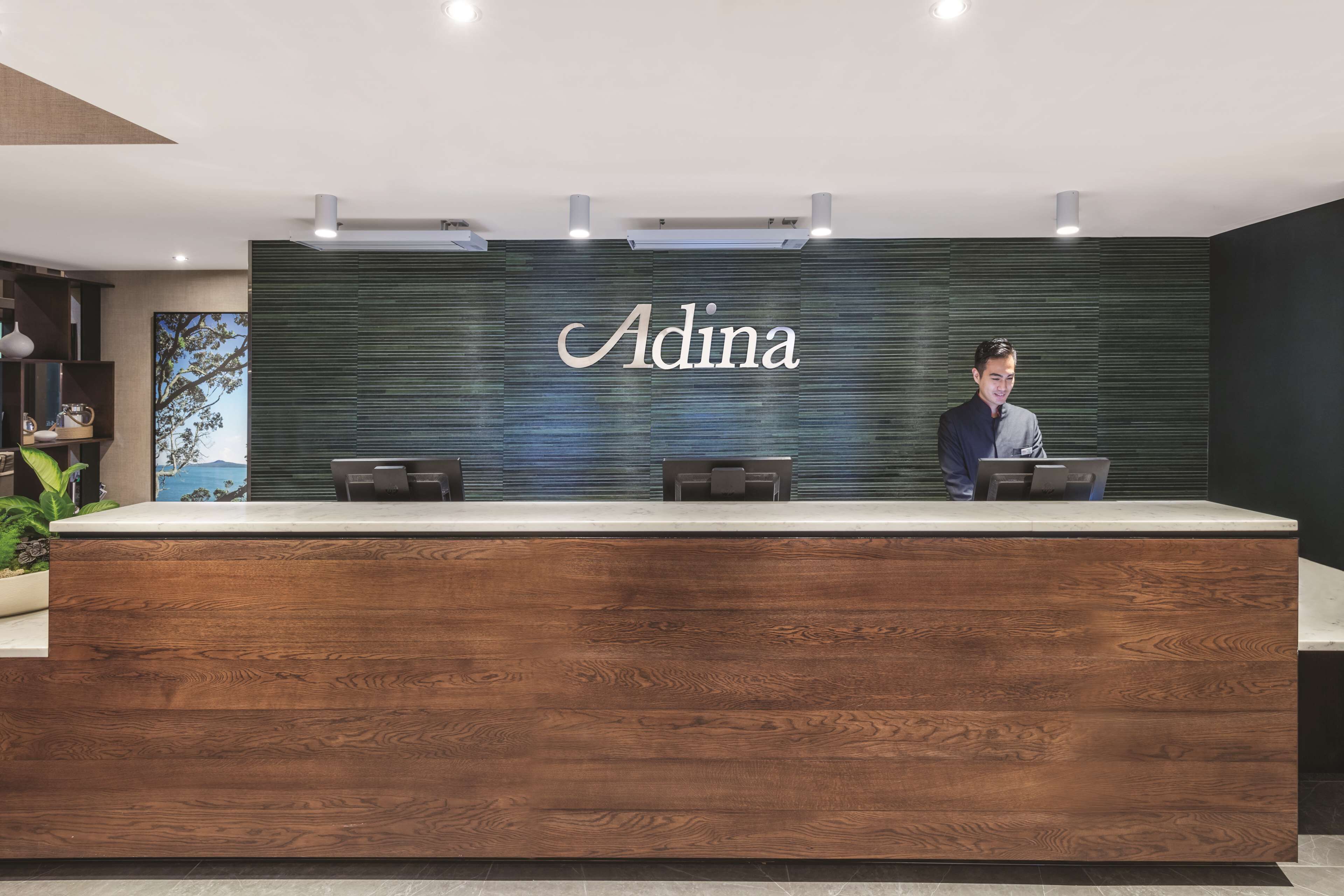 A reception desk with a wooden finish and a nameplate that reads "Adina."