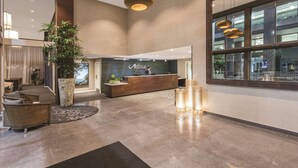 Een moderne hotellobby met een receptiebalie, een zithoek en grote ramen.