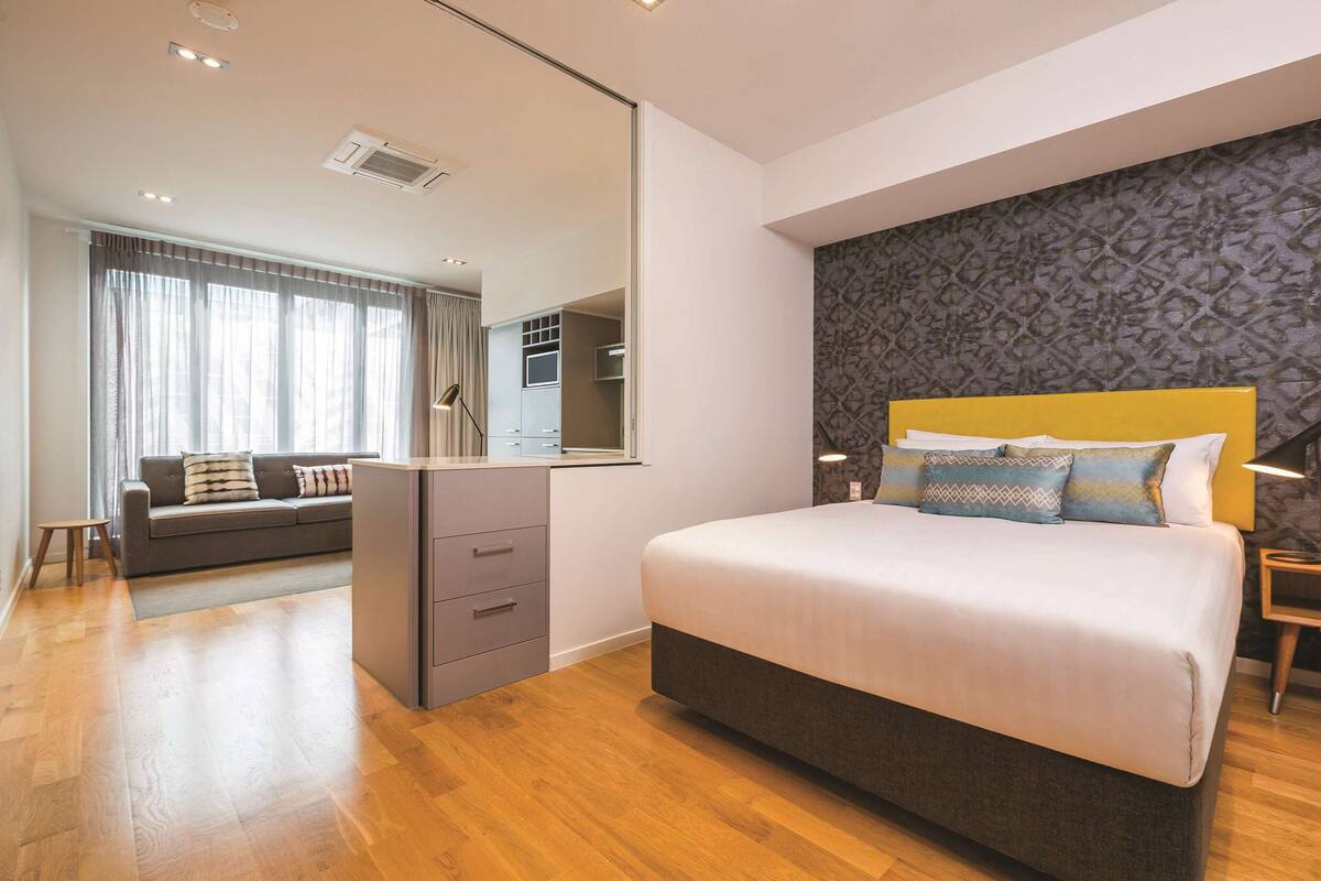 Ein modernes Hotelzimmer mit einem großen Bett, einer Couch, einem Kleiderschrank und einem Spiegel.