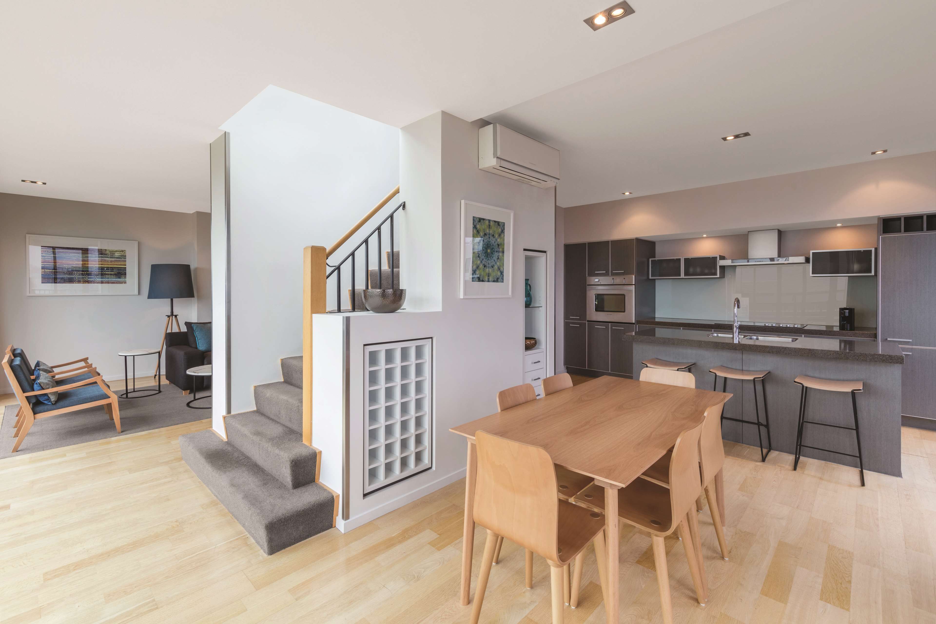 A modern apartment with a wooden dining table, a kitchen with dark cabinets, and a staircase leading to a loft area.