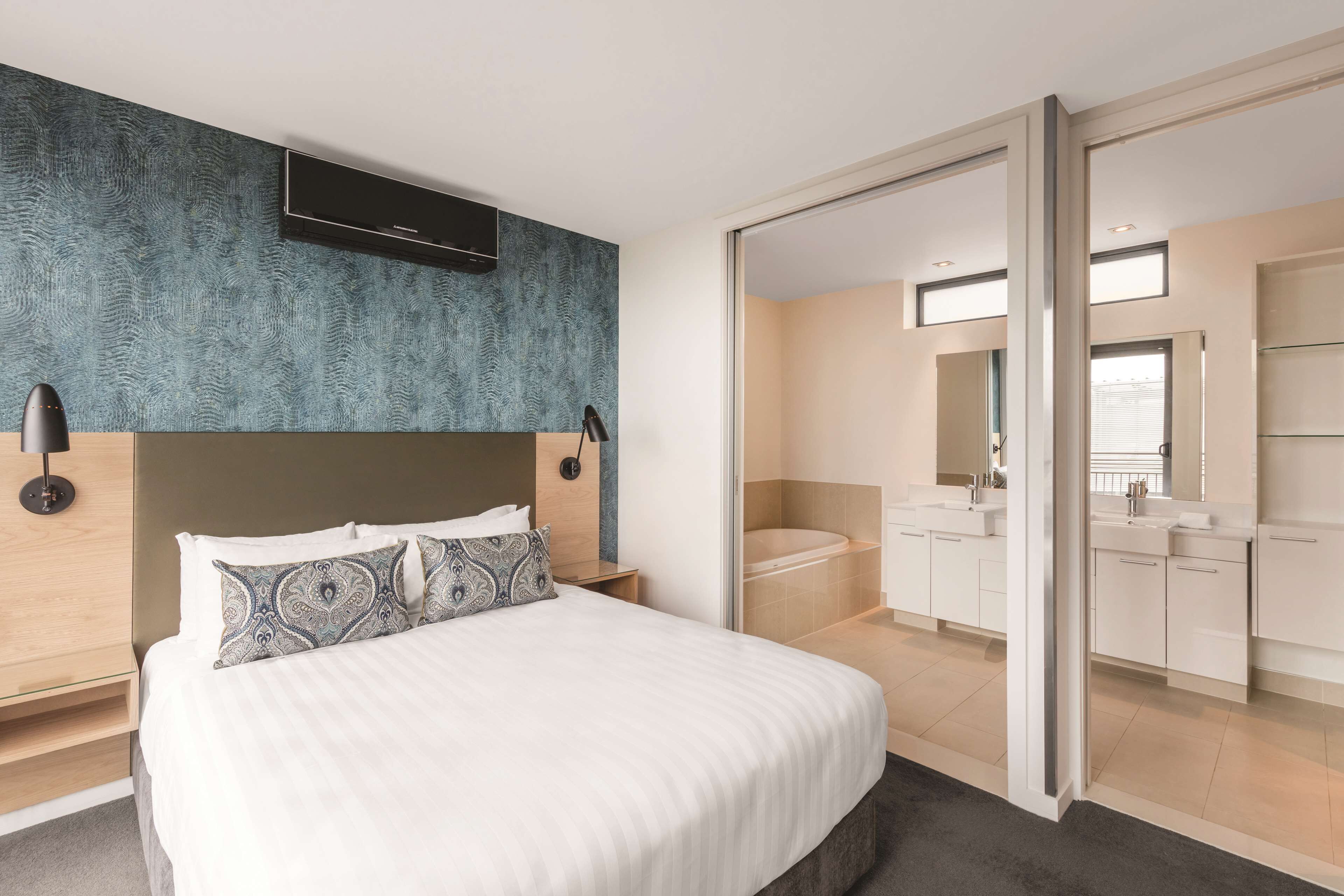 Een moderne hotelkamer met een groot bed, een aan de muur bevestigde televisie en een badkamer met een bad en wastafel.