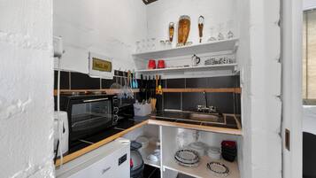 Cocina compacta con microondas, horno y lavamanos. Se observan estantes con cristalería y utensilios.