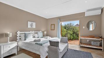 A bedroom with a bed, nightstands, a dresser, a mirror, and a view of greenery outside.