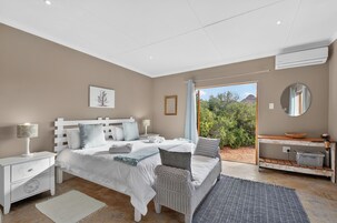 A bedroom with a bed, nightstands, a dresser, a mirror, and a view of greenery outside.