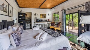 Een kamer met een groot bed, een kitchenette, een eethoek en uitzicht op groen.