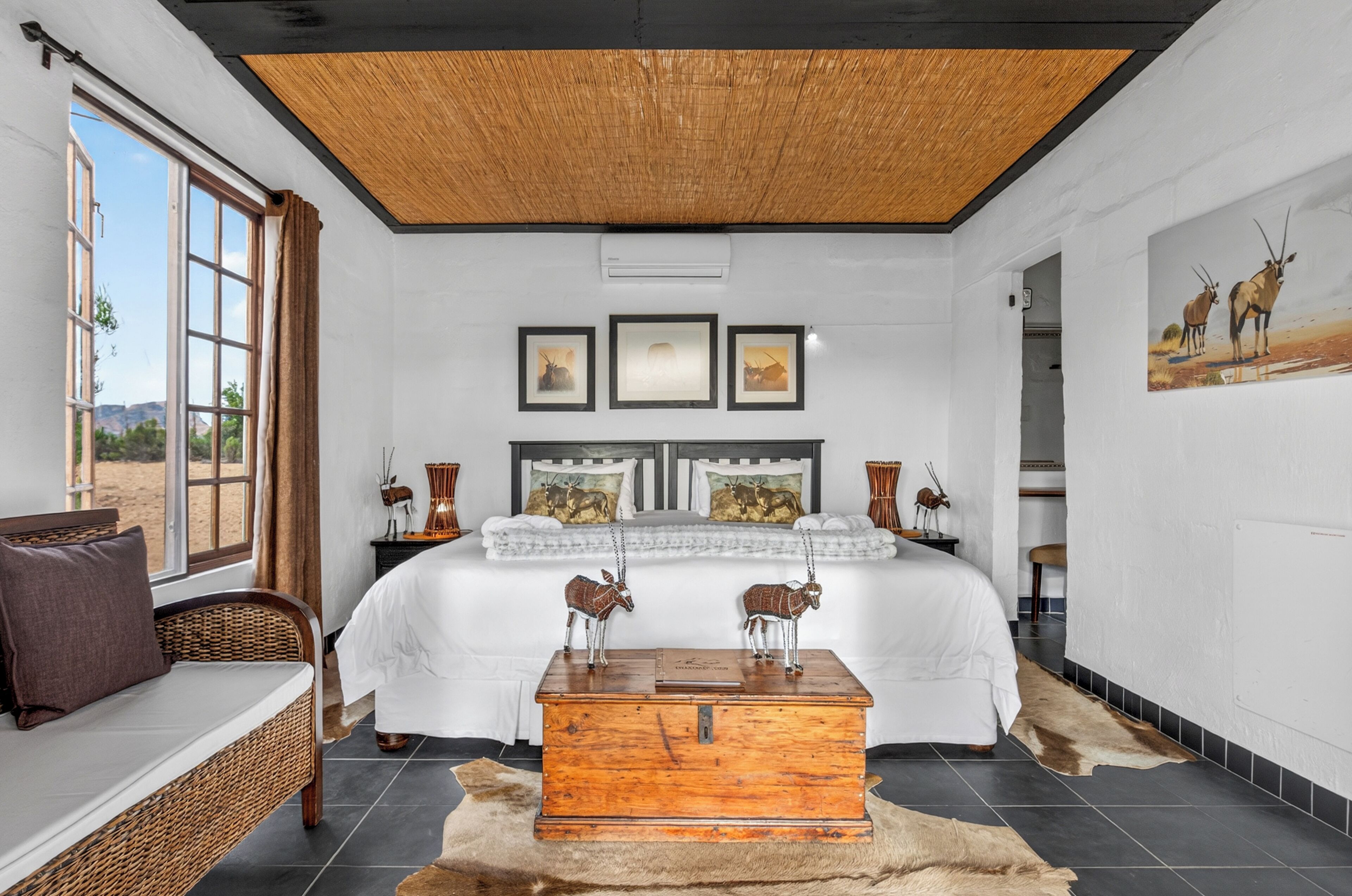 A bedroom with a large bed, a wooden chest, and a view of the outdoors.